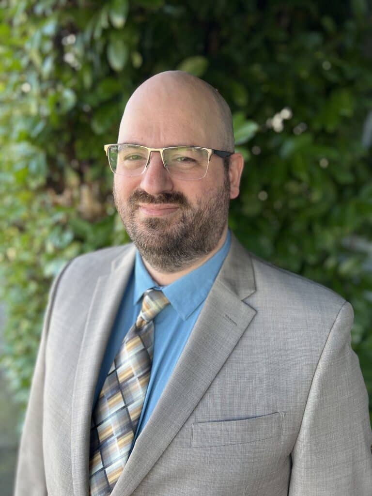 Man in suit with greenery background.