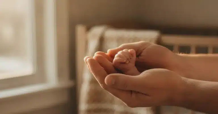 Blog 5 Photorealistic image: a pair of adult hands gently holding a tiny infant's hand against a warm, softly lit background with na