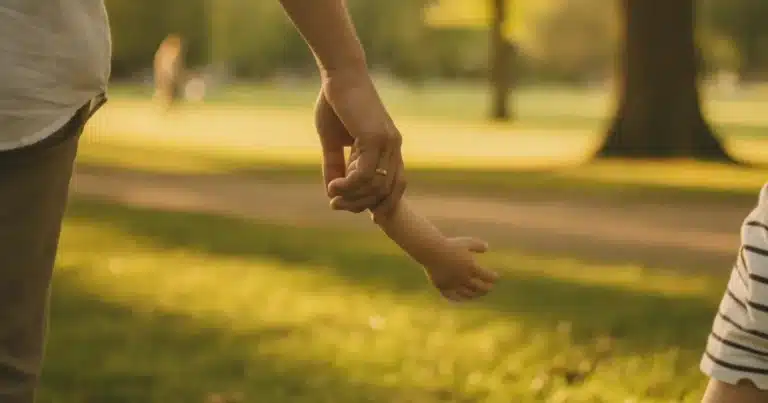 Photorealistic image of a parent's hand gently holding a small child's hand while walking through a sunny park, warm natural
